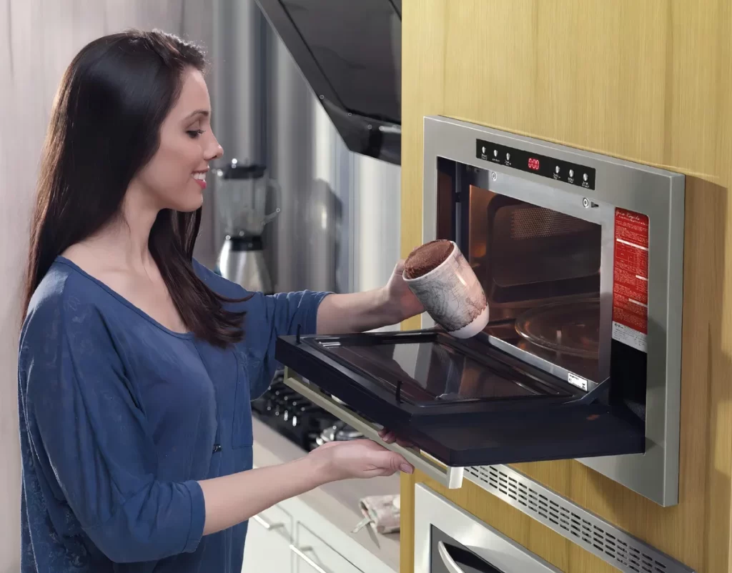 mulher tira uma caneca do forno micro-ondas de embutir